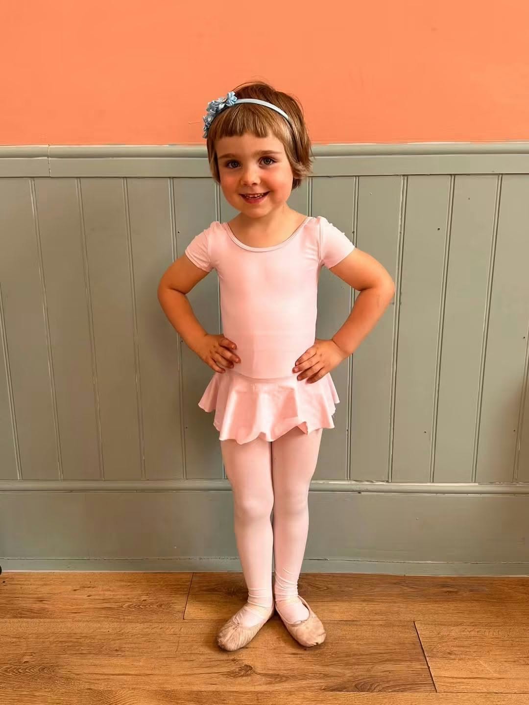 A young dancer in a pink ballet outfit standing with hands on hips